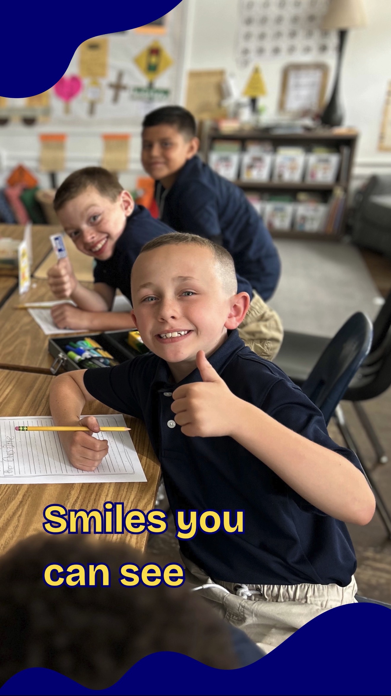 3 school children sitting at desks smiling , "Smiles you can see" displayed in text on screen